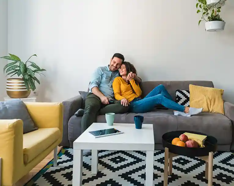 Couple sitting on a couch smiling confidently at having dental implant insurance.