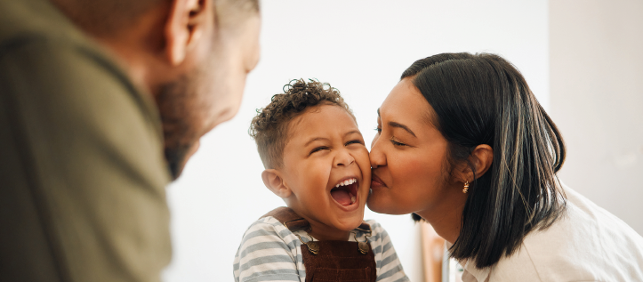 A child smiling while getting a big kiss from their mother