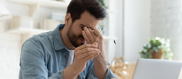 A man rubbing his eyes while holding his glasses