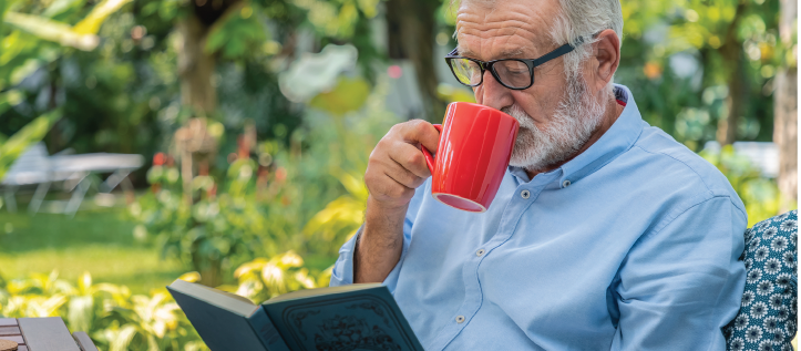 An older man drinking his coffee while reading a book