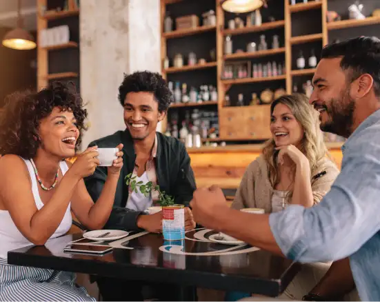 A group of young adults smiling and enjoying themselves at a coffee shop.