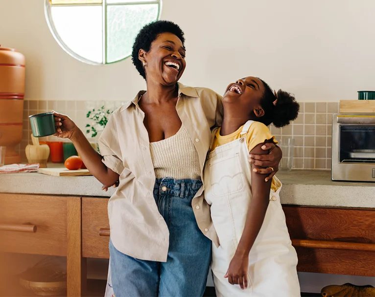A woman and her daughter smiling in their kitchen