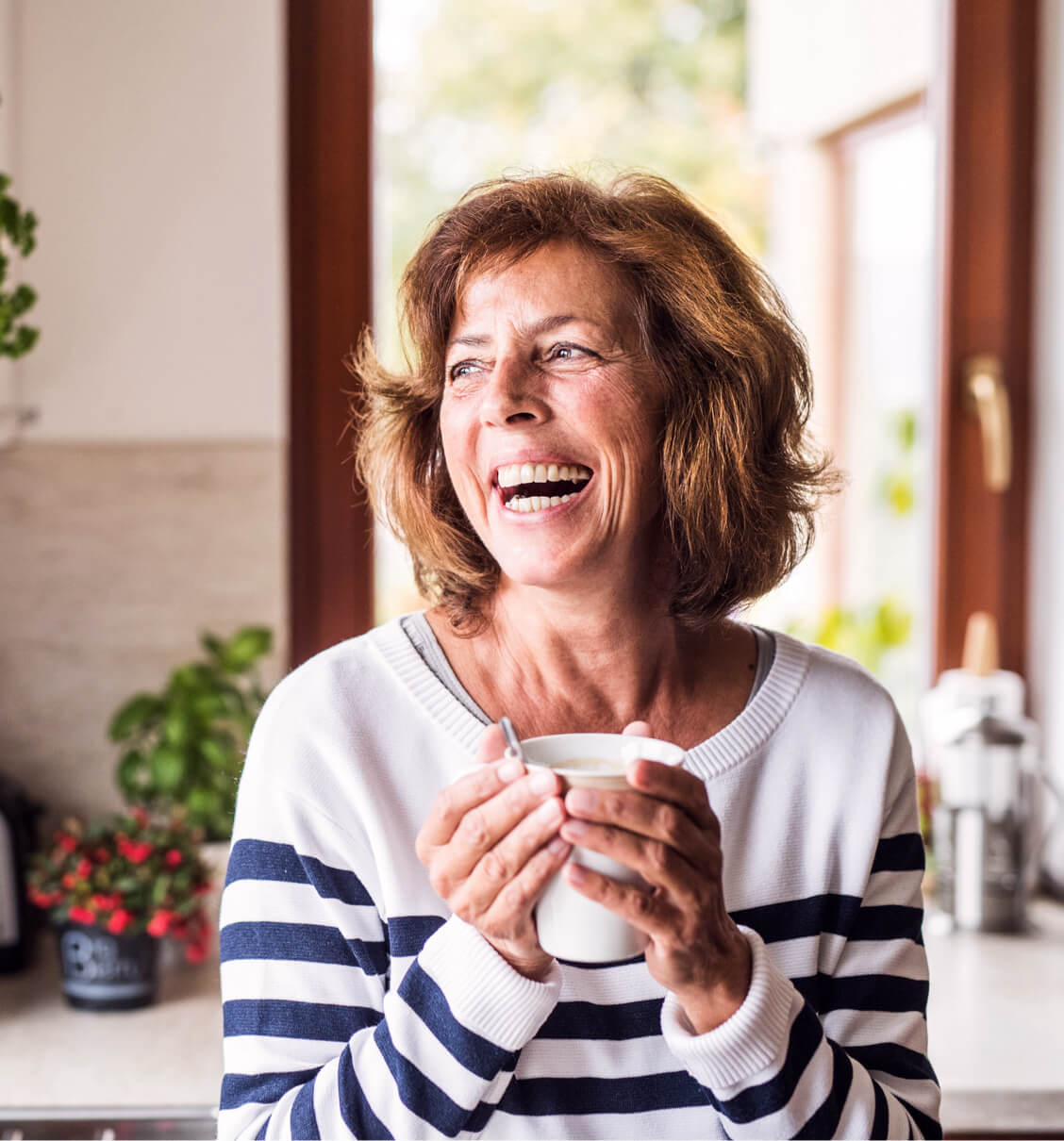 Three friends smiling, looking at a phone and enjoying beverages, with happy, confident smiles, with Spirit Dental coverage.