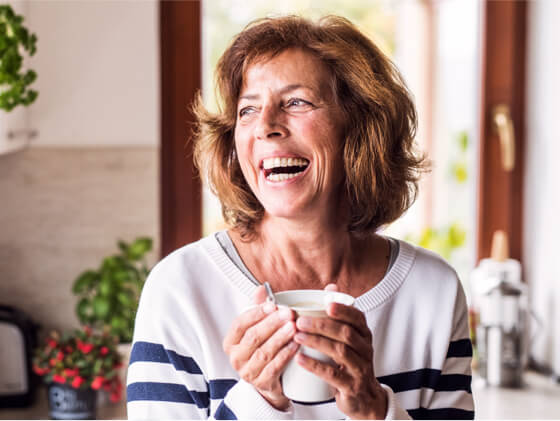 Three friends smiling, looking at a phone and enjoying beverages, with happy, confident smiles, with Spirit Dental coverage.